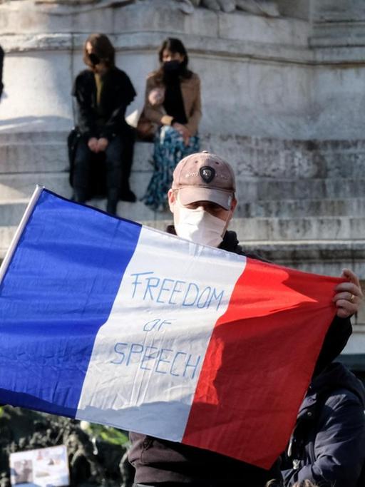Ein Demonstrant mit der französische Flagge in den Händen. Auf der Flagge steht die Aufschrift "Redefreiheit".