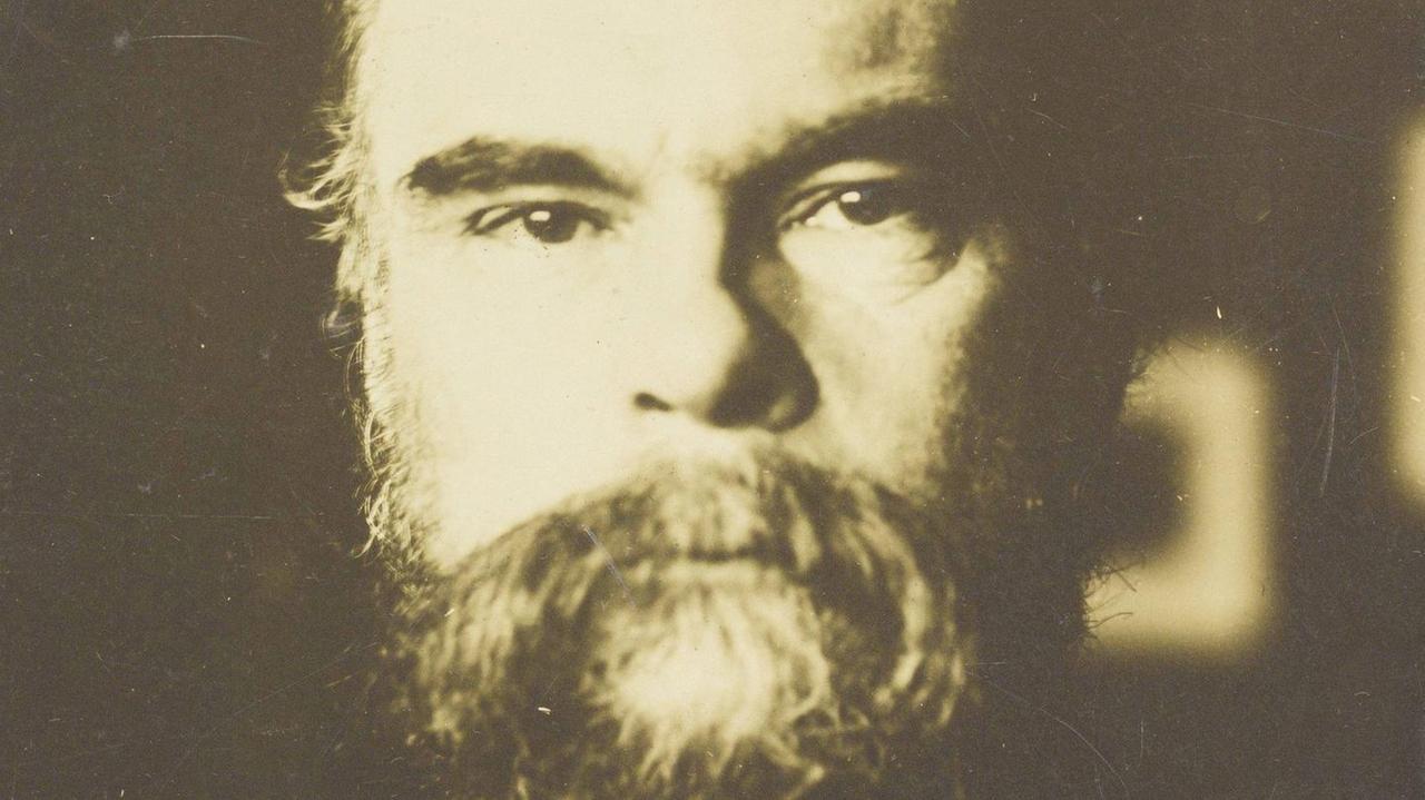 Eine alte braun-graue Fotografie eines Mannes mittleren Alters mit großem Vollbart, der ernst in die Kamera blickt. Eine alte braun-graue Fotografie eines Mannes mittleren Alters mit großem Vollbart, der ernst in die Kamera blickt.