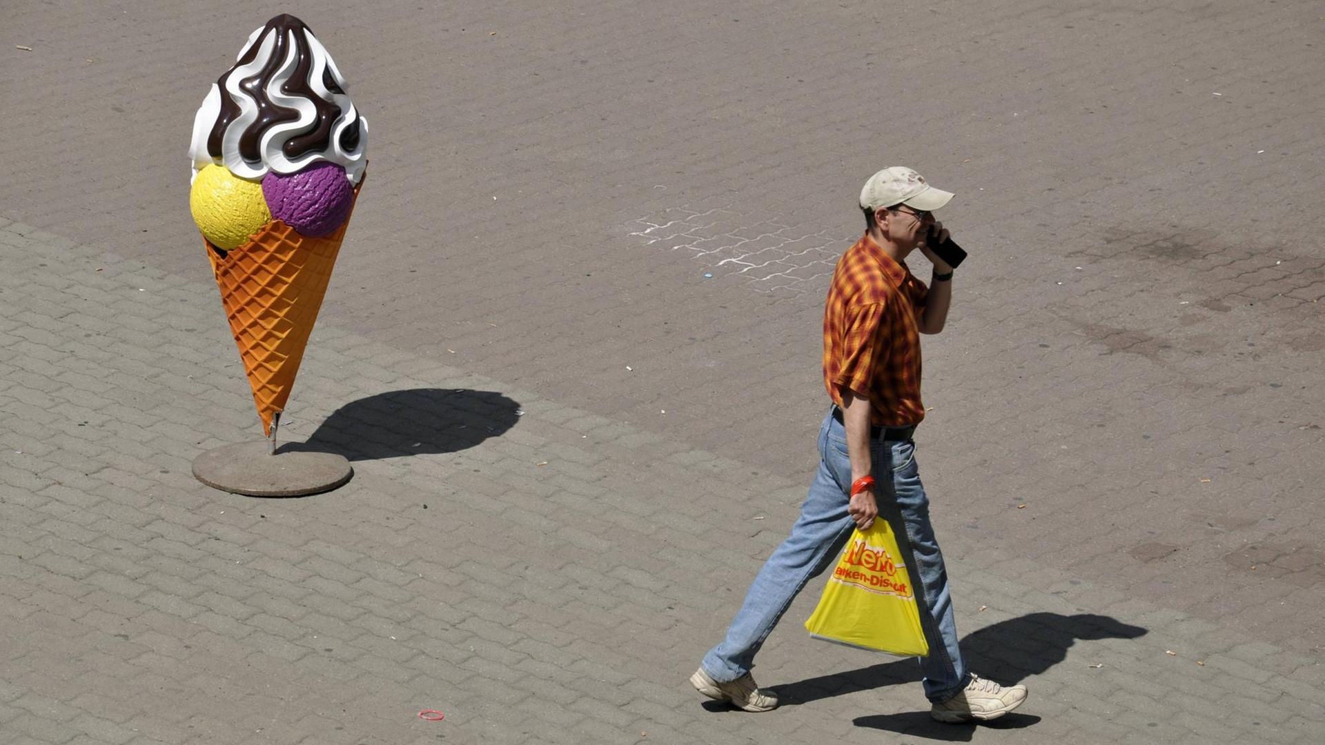 Ein Fußgänger mit Telefon und Einkaufstüte geht an einer Werbe-Eistüte vorbei Ein Fußgänger mit Telefon und Einkaufstüte geht an einer Werbe-Eistüte vorbei
