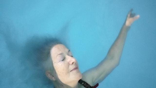 Eine ältere Frau treibt mit geschlossenen Augen auf dem Wasser eines Schwimmbeckens.