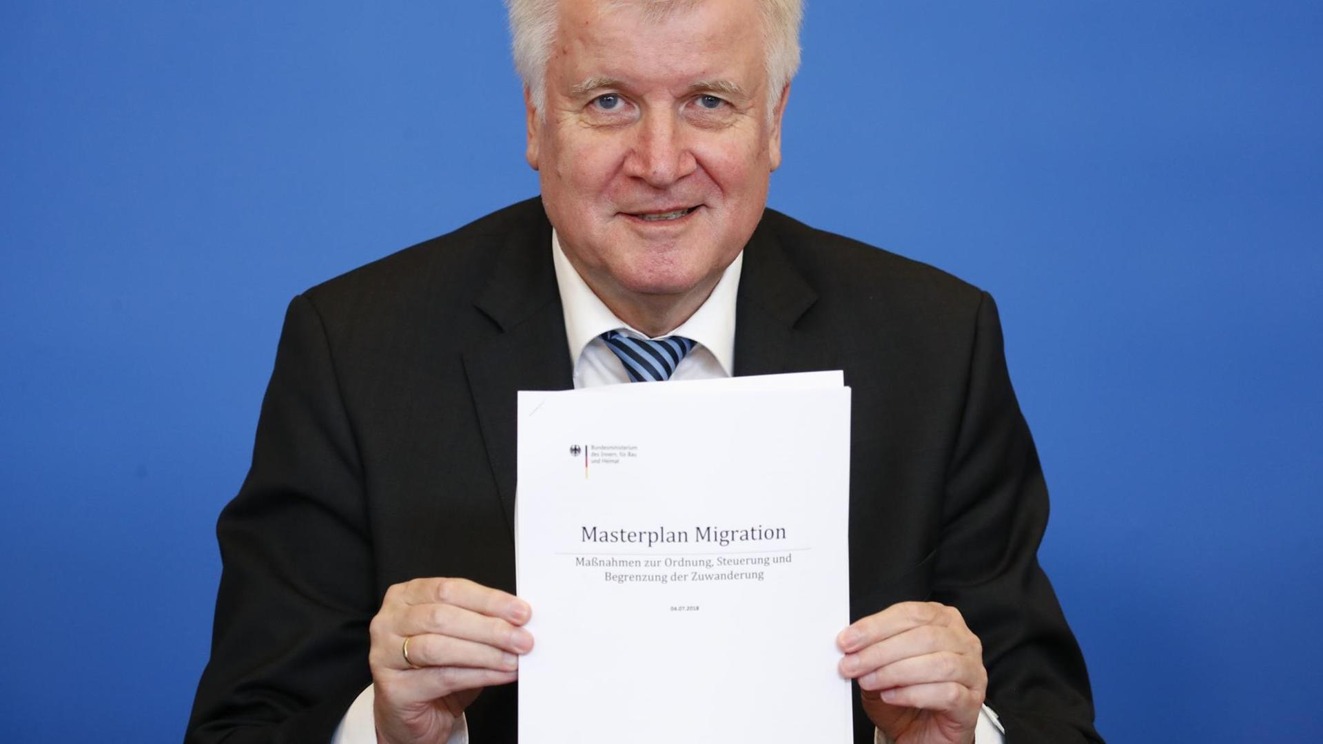 Seehofer hält ein Exemplar des "Masterplan Migration" in die Kamera.