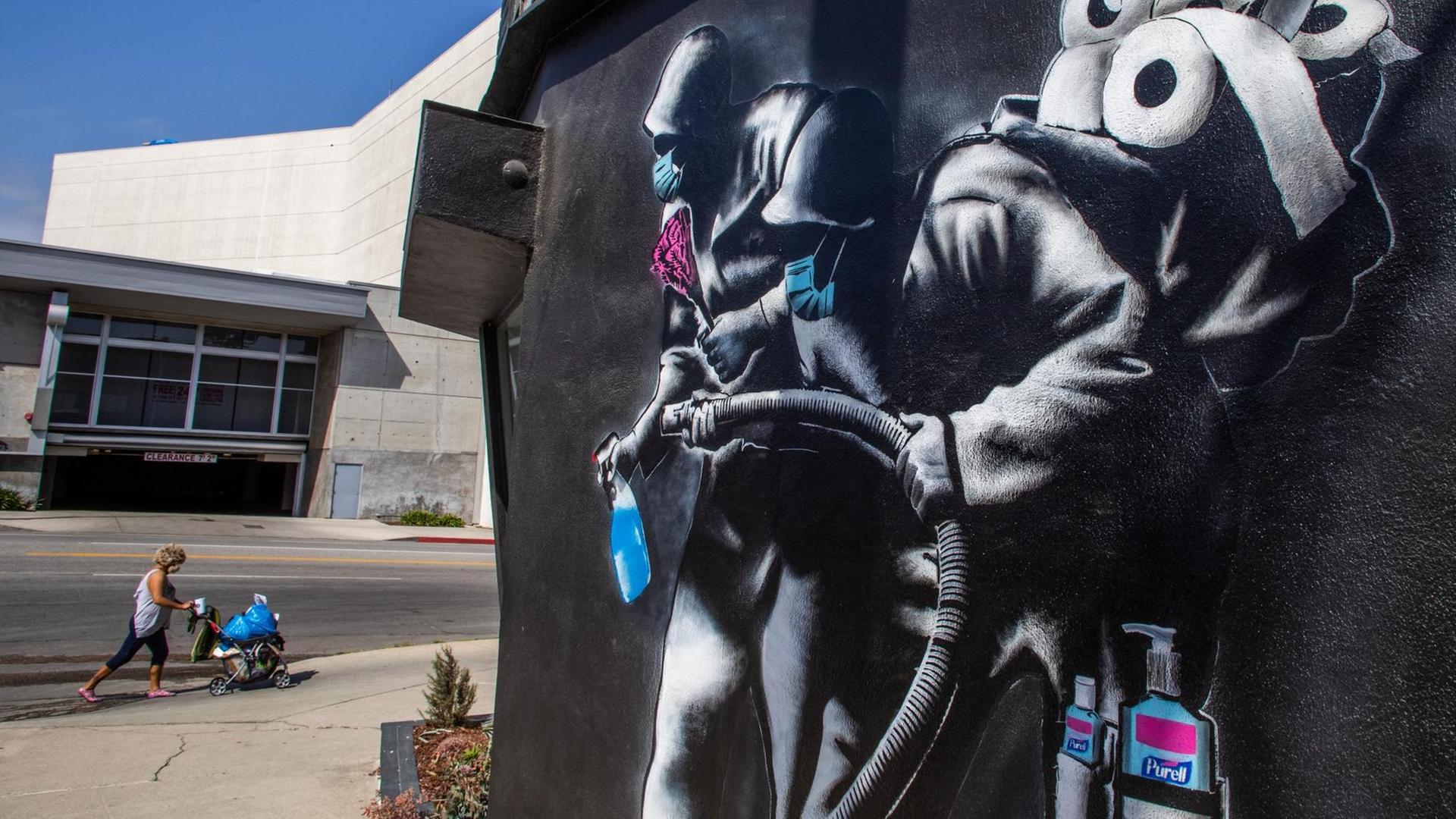Eine Frau läuft an einem Wandgemälde von 'Hijackhart' vorbei. Es zeigt Soldaten, die desinfizieren. Los Angeles, Kalifornien, 2020. Eine Frau läuft an einem Wandgemälde von 'Hijackhart' vorbei. Es zeigt Soldaten, die desinfizieren. Los Angeles, Kalifornien, 2020.