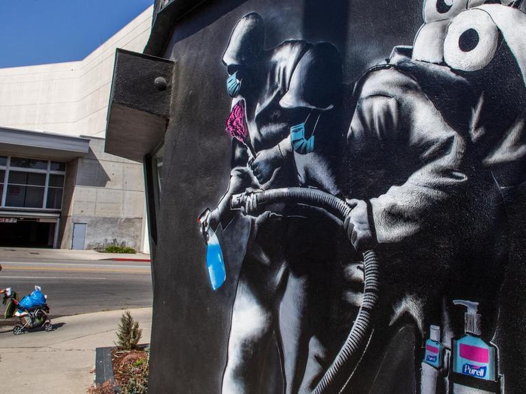 Eine Frau läuft an einem Wandgemälde von 'Hijackhart' vorbei. Es zeigt Soldaten, die desinfizieren. Los Angeles, Kalifornien, 2020.