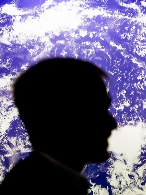 Ein Mann sitzt bei der UN-Klimakonferenz COP26 vor einem leuchtenden Globus.