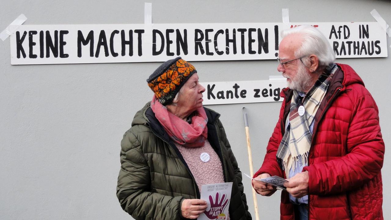 Eine ältere Frau und ein älterer Mann von der Initiative "Omas gegen Rechts" unterhalten sich auf einem Marktplatz in Hamburg. Im Hintergrund ist der Schriftzug "Keine Macht den Rechten!" zu sehen.