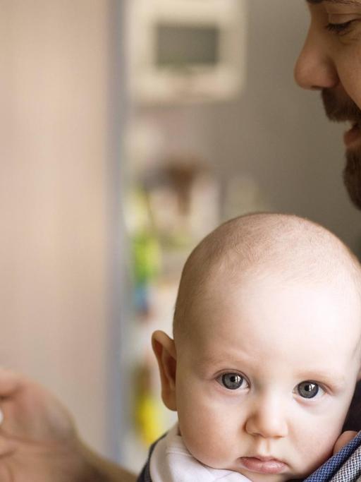 Ein Vater trägt ein Baby an der Brust und schaut dabei auf sein Smartphone