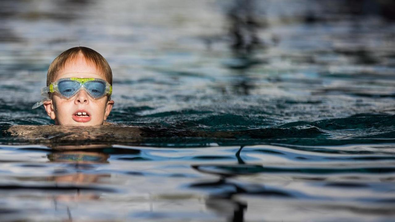 Ein Junge im Grundschul-Alter schwimmt in einem Schwimm-Bad Ein Junge im Grundschul-Alter schwimmt in einem Schwimm-Bad