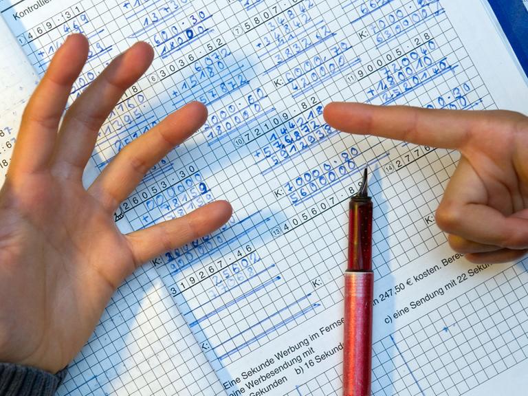 Ein Grundschüler nimmt bei den Hausaufgaben im Fach Mathematik seine Finger zur Hilfe.