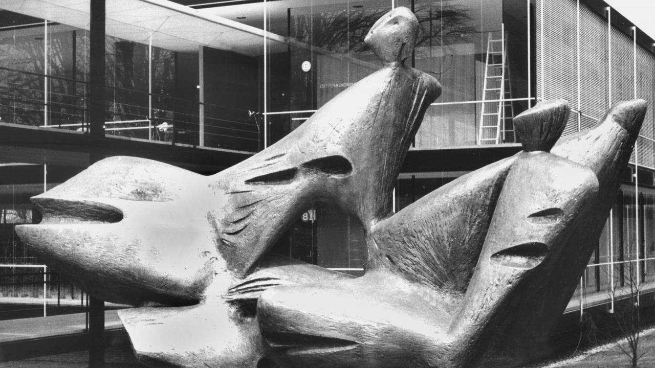 Schwarzweiß Fotografie von Bern Heiliger  vor seiner Skulptur 
"Mensch und Fortschritt" die er  im Auftrag der Bundesregierung geschaffen hat und die vor dem deutschen Pavillon installiert wurde. Am 17. April 1958 wurde in der belgischen Hauptstadt Brüssel die erste Weltausstellung nach dem Zweiten Weltkrieg eröffnet. 