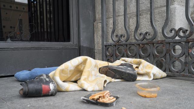 Lagerplatz eines Obdachlosen mit zerrissenen Schuhen, Essensresten und einer Decke vor einem Geschäft in Madrid.