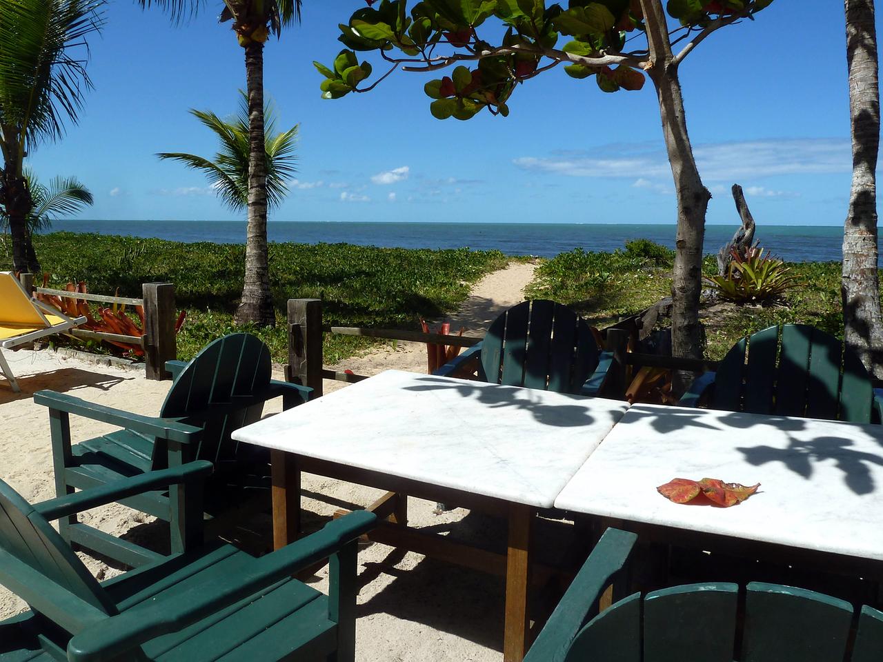 Tische und Stühle stehen auf eine Veranda unter Bäumen und mit Blick auf den Strand und das Meer. Tische und Stühle stehen auf eine Veranda unter Bäumen und mit Blick auf den Strand und das Meer.