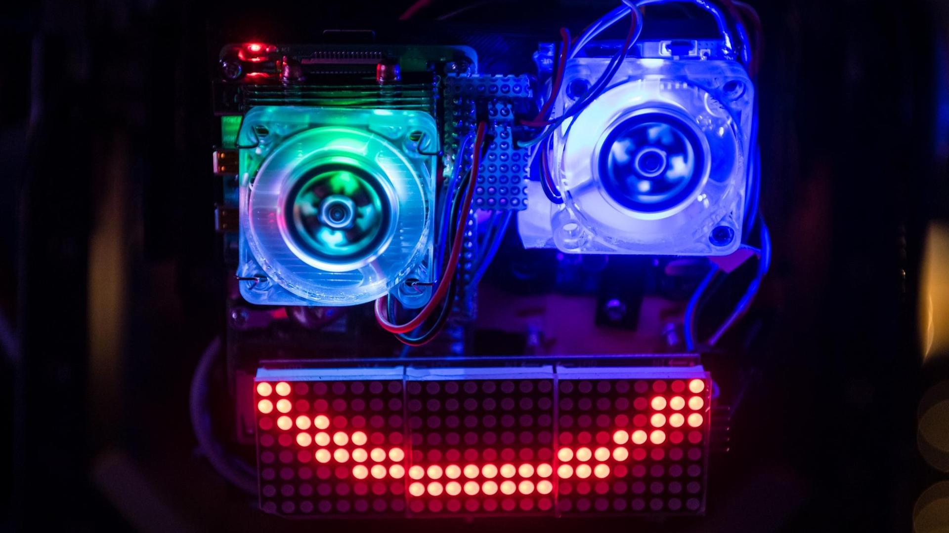 Eine in blau und grün beleuchtete Installation eines Gesichtes aus Computerbauteilen mit rot leuchtendem Mund.