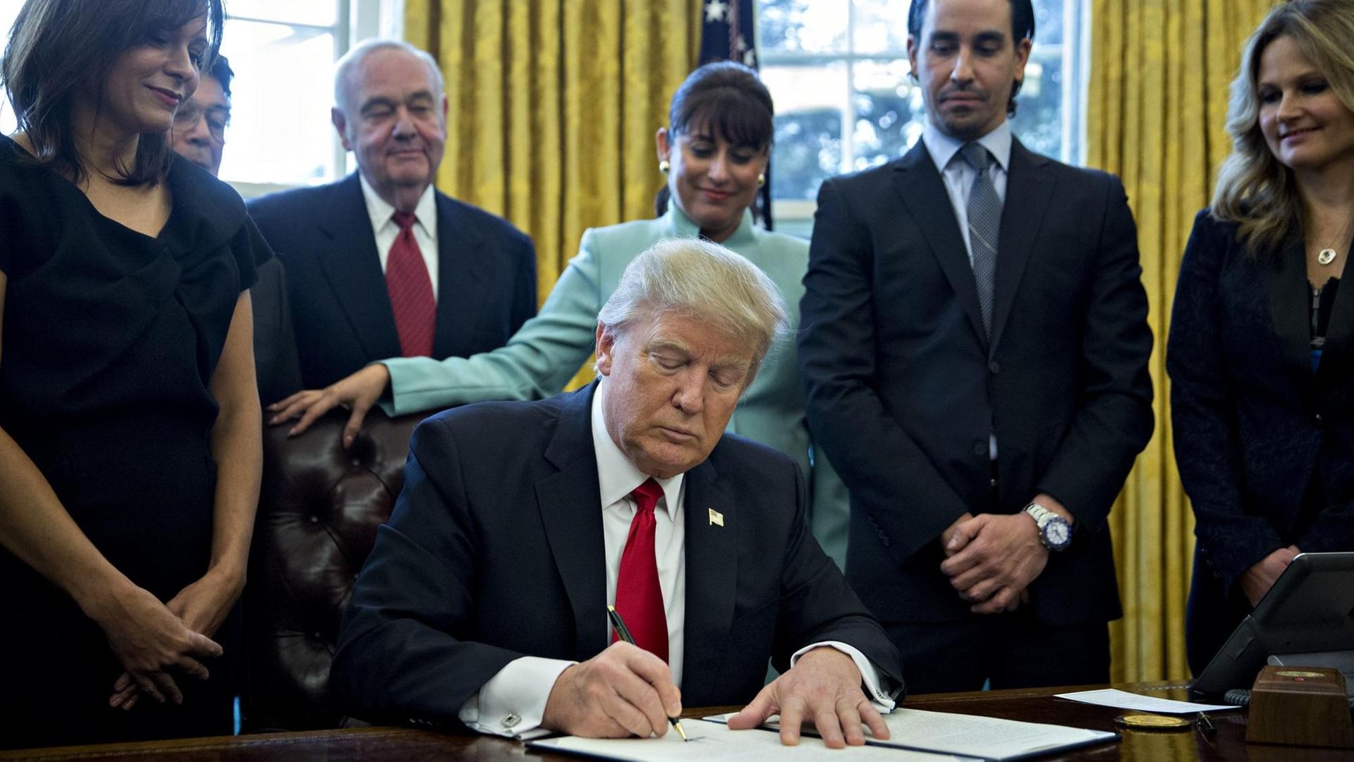 Trump am Schreibtisch, umringt von Managern. Er unterschreibt den Erlass. Trump am Schreibtisch, umringt von Managern. Er unterschreibt den Erlass.