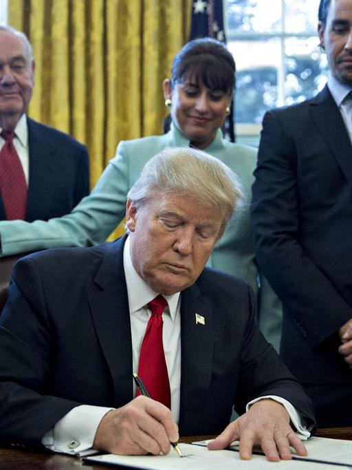 Trump am Schreibtisch, umringt von Managern. Er unterschreibt den Erlass.
