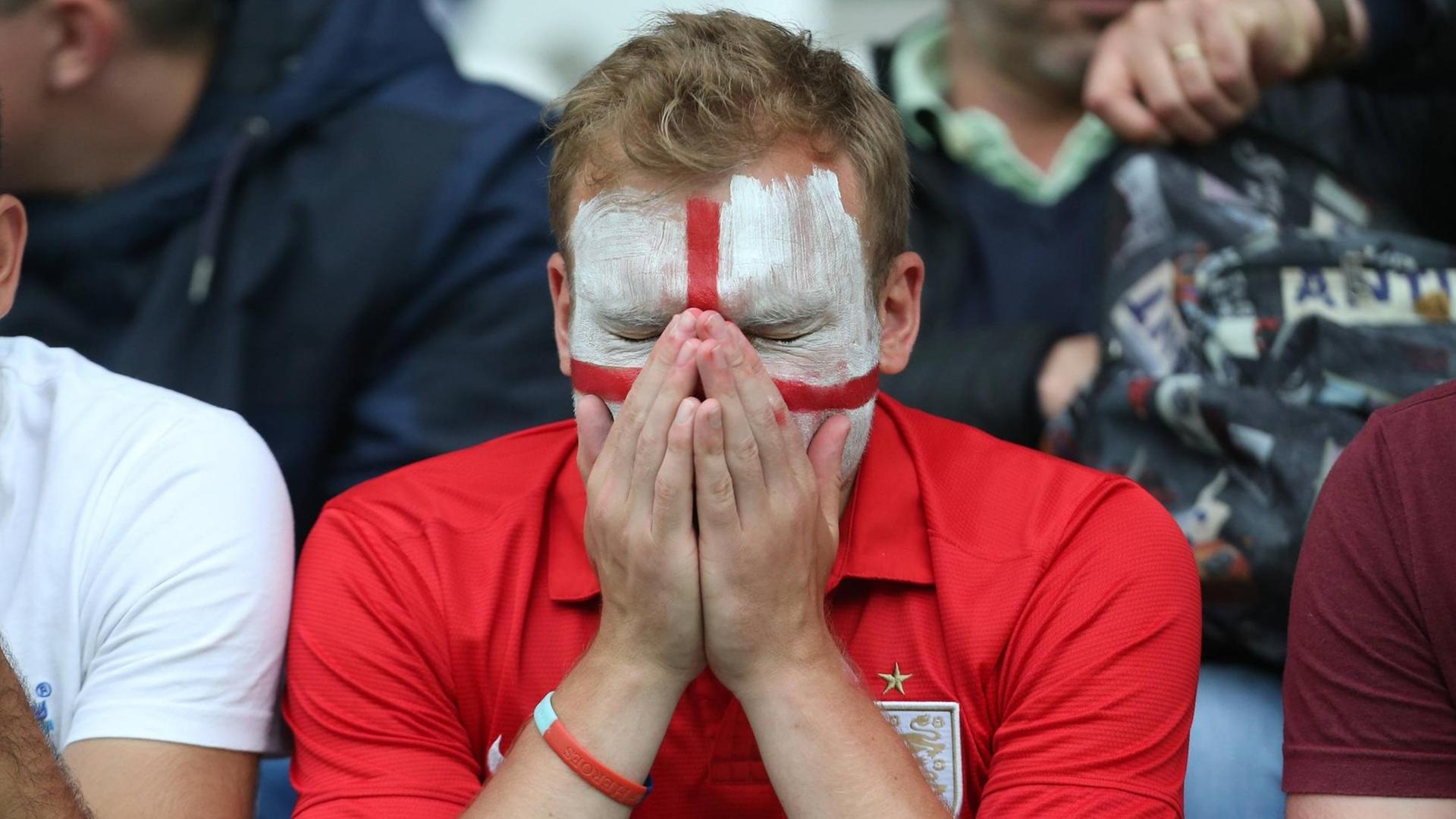 Ein England-Fan mit englischer Flagge als Gesichtsbemalung hält die Hände ins Gesicht. Ein England-Fan mit englischer Flagge als Gesichtsbemalung hält die Hände ins Gesicht.