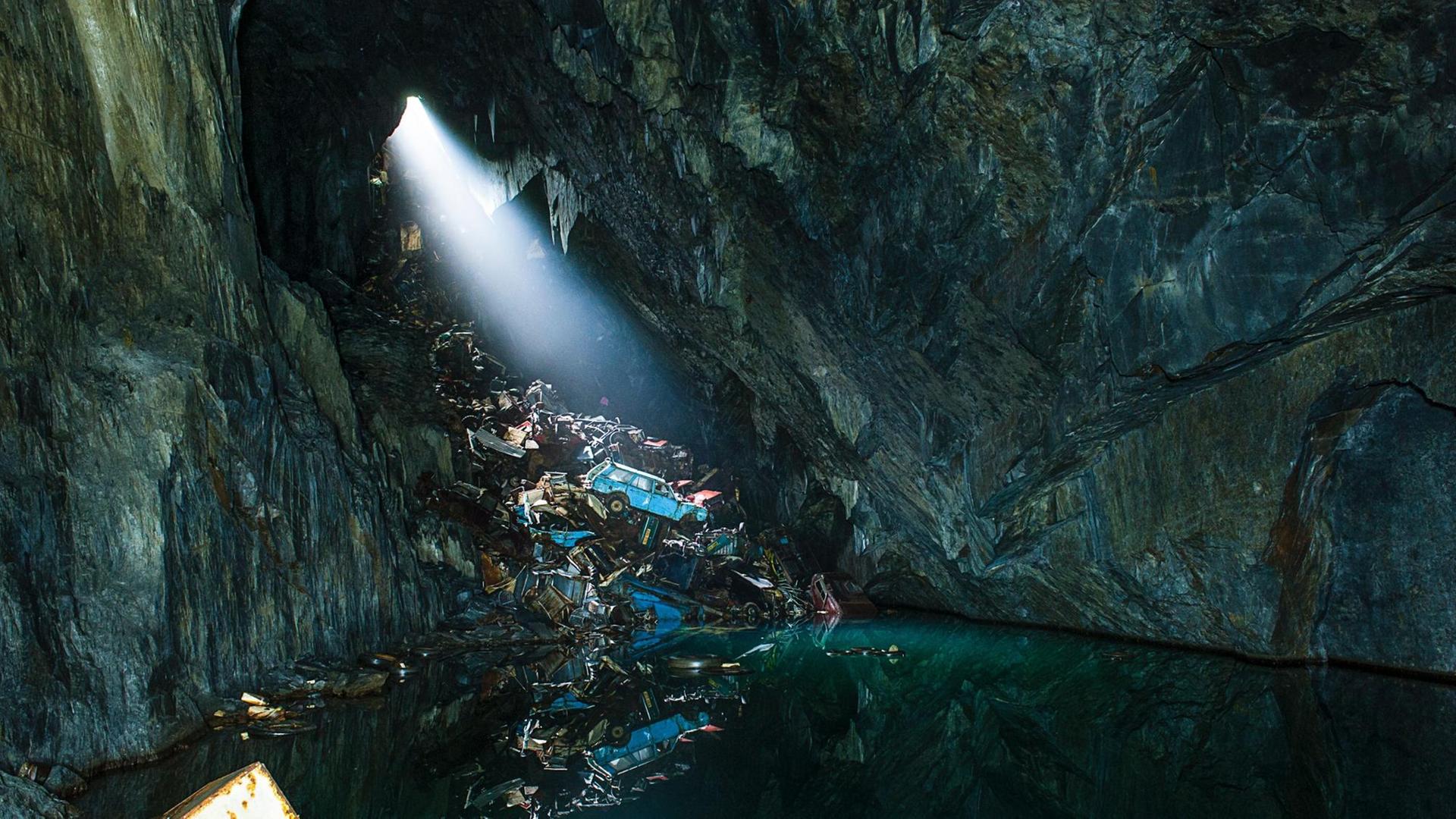 Höhle mit Wasser und einem Spalt im Stein, durch den Sonnenlicht auf einen Müllhaufen fällt