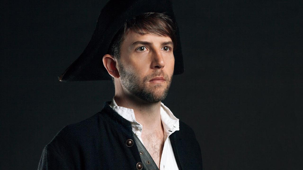 Owen Pallett steht mit weißem Hemd und schwarzer Jacke vor einem schwarzen Hintergrund Owen Pallett steht mit weißem Hemd und schwarzer Jacke vor einem schwarzen Hintergrund