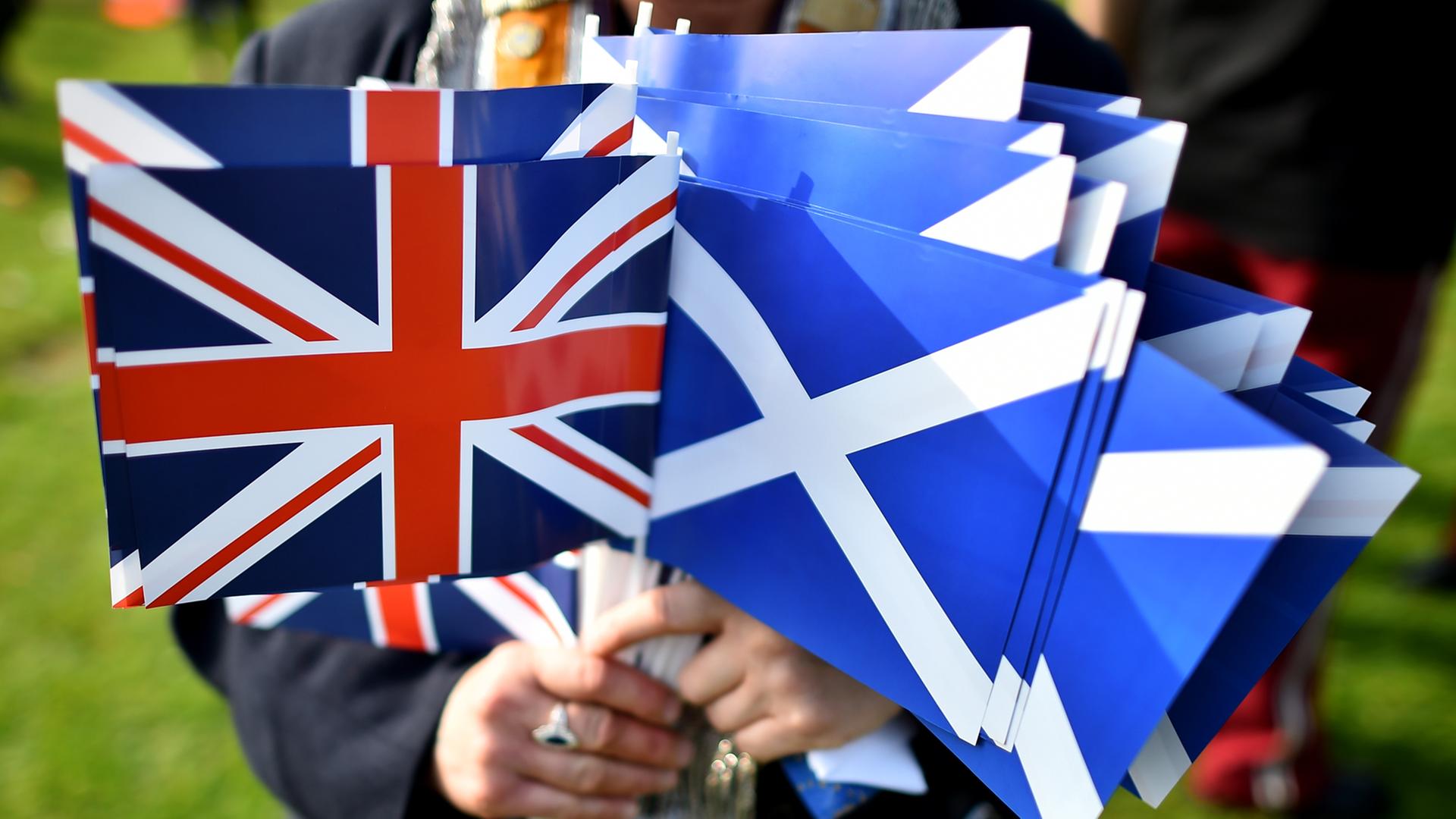 Eine Person hält mehrere Papierflaggen in der Hand. Sowohl welche mit Schottlands Wappen als auch dem Union Jack. Eine Person hält mehrere Papierflaggen in der Hand. Sowohl welche mit Schottlands Wappen als auch dem Union Jack.