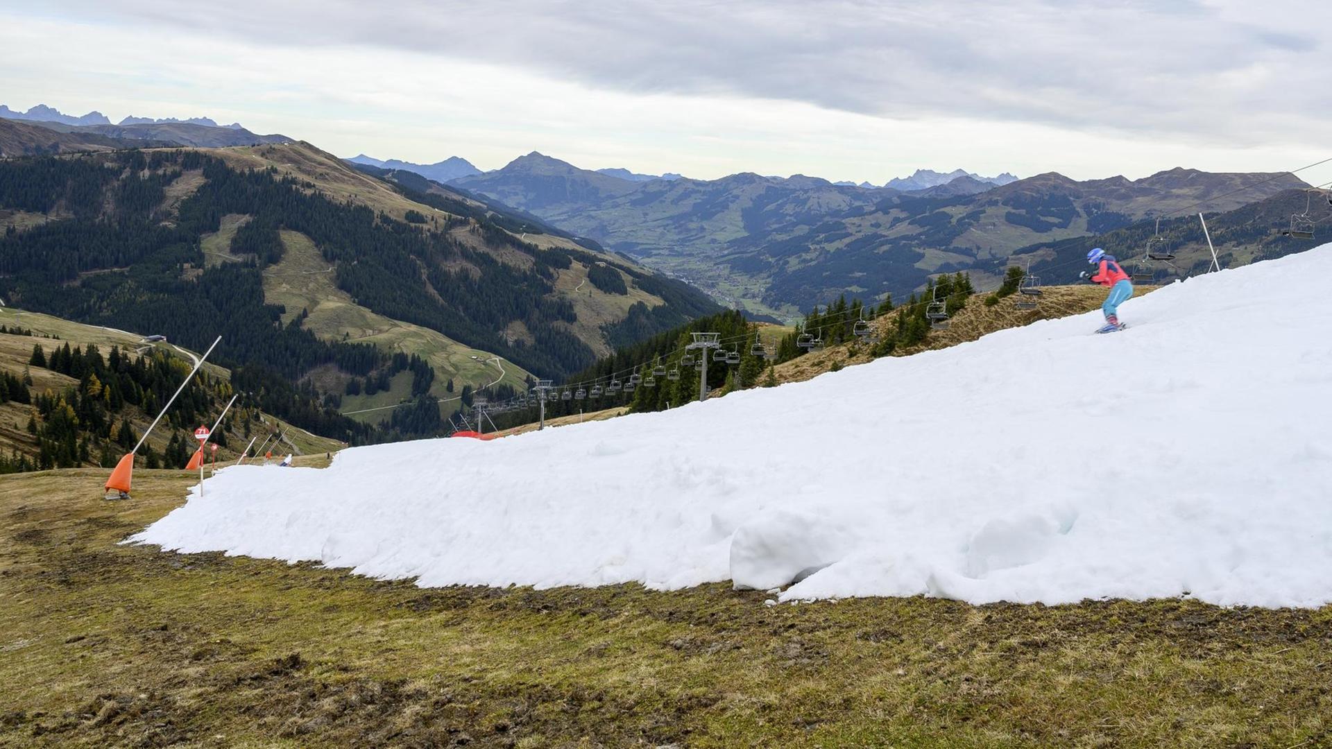 Das Bild zeigt einen Skifahrer auf einem weißen Kunstschneeband in einer grünen und braunen Herbstlandschaft. Aufgenommen im Skigebiet Resterhoehe von Kitzbühel bei Mittersill, Österreich. Der frühe Start der Skisaison auf einer Kitzbüheler Piste am Wochenende löste eine hitzige Debatte zwischen Klimaaktivisten und Beamten im berühmten österreichischen Ferienort aus.