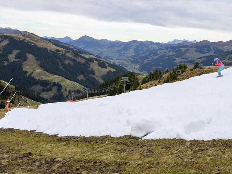 Das Bild zeigt einen Skifahrer auf einem weißen Kunstschneeband in einer grünen und braunen Herbstlandschaft. Aufgenommen im Skigebiet Resterhoehe von Kitzbühel bei Mittersill, Österreich. Der frühe Start der Skisaison auf einer Kitzbüheler Piste am Wochenende löste eine hitzige Debatte zwischen Klimaaktivisten und Beamten im berühmten österreichischen Ferienort aus.