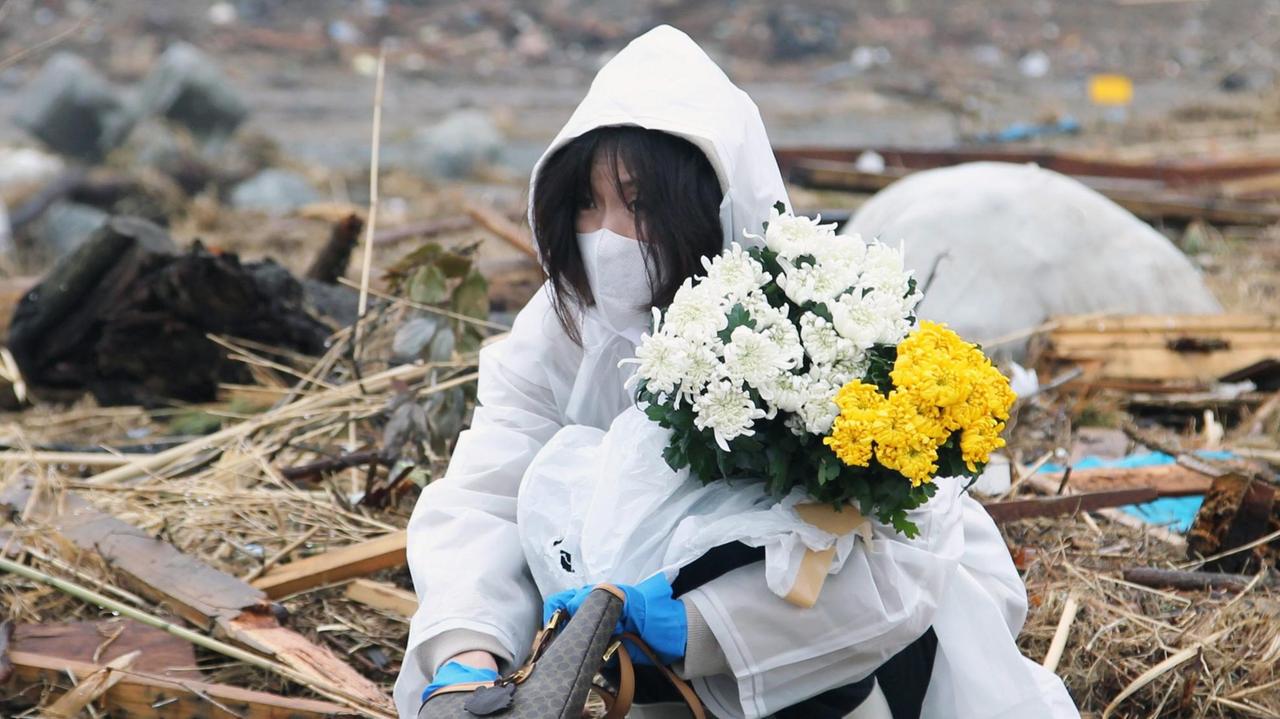 Eine Frau betet und legt Blumen nieder an der Stelle an der ihr Haus stand, das durch den Tsunami, der auch das nahegelegene Kernkraftwerk Fukushima beschädigt hat, zerstört wurde. 