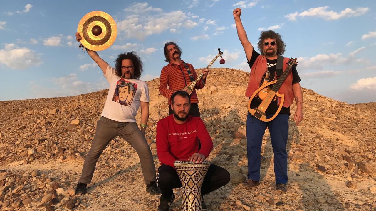 Vier Männer stehen mit ihren türkischen Musikinstrumenten auf einem Steinhügel.