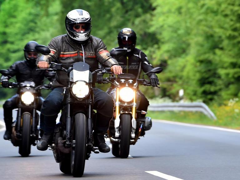 Drei Motorradfahrer in voller Montur fahren auf einer Straße