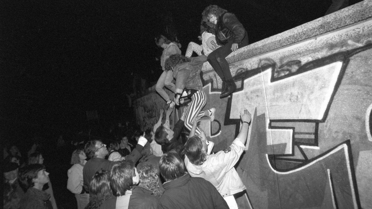 Menschen klettern am späten Abend des 09.11.1989 auf die Berliner Mauer am Brandenburger Tor. Am Abend des 09.11.1989 teilte SED-Politbüro Mitglied Günter Schabowski mit, daß alle DDR-Grenzen in die Bundesrepublik und nach West-Berlin für DDR-Bürger geöffnet werden. Daraufhin strömten binnen weniger Stunden tausende von Ost-Berlinern in den Westteil der Stadt, wo es zu volksfestartigen Verbrüderungen zwischen Bürgern aus Ost- und Westdeutschland kam | Verwendung weltweit Menschen klettern am späten Abend des 09.11.1989 auf die Berliner Mauer am Brandenburger Tor. Am Abend des 09.11.1989 teilte SED-Politbüro Mitglied Günter Schabowski mit, daß alle DDR-Grenzen in die Bundesrepublik und nach West-Berlin für DDR-Bürger geöffnet werden. Daraufhin strömten binnen weniger Stunden tausende von Ost-Berlinern in den Westteil der Stadt, wo es zu volksfestartigen Verbrüderungen zwischen Bürgern aus Ost- und Westdeutschland kam | Verwendung weltweit