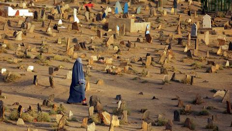 Eine Frau läuft zwischen Gräbern über einen Friedhof in Kabul.