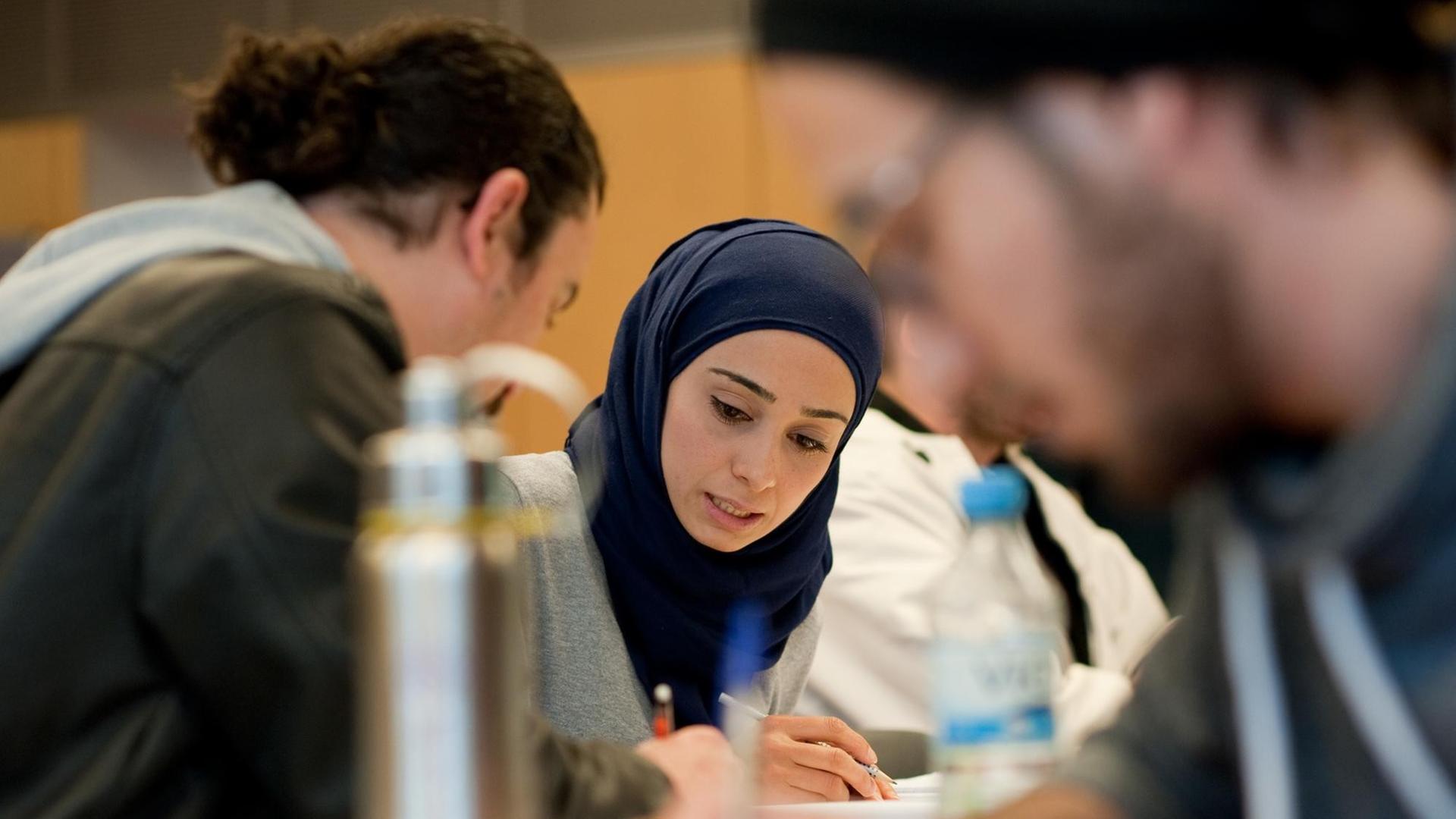Ein junge Lehrerin aus Syrien löst am 14.04.2016 in Potsdam (Brandenburg) in einem Hörsaal des Campus Griebnitzsee der Universität Potsdam während des Deutschunterrichts zusammen mit weiteren Schülern eine Aufgabe.