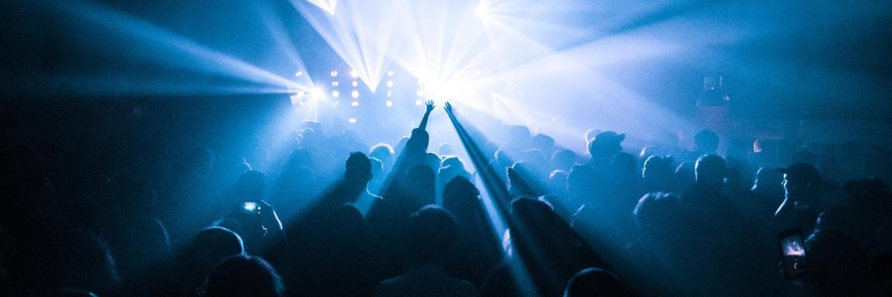 Menschen, die im Club tanzen und ihre Hände in die Höhe werfen; die Szene ist in blaues Laserlicht getaucht.