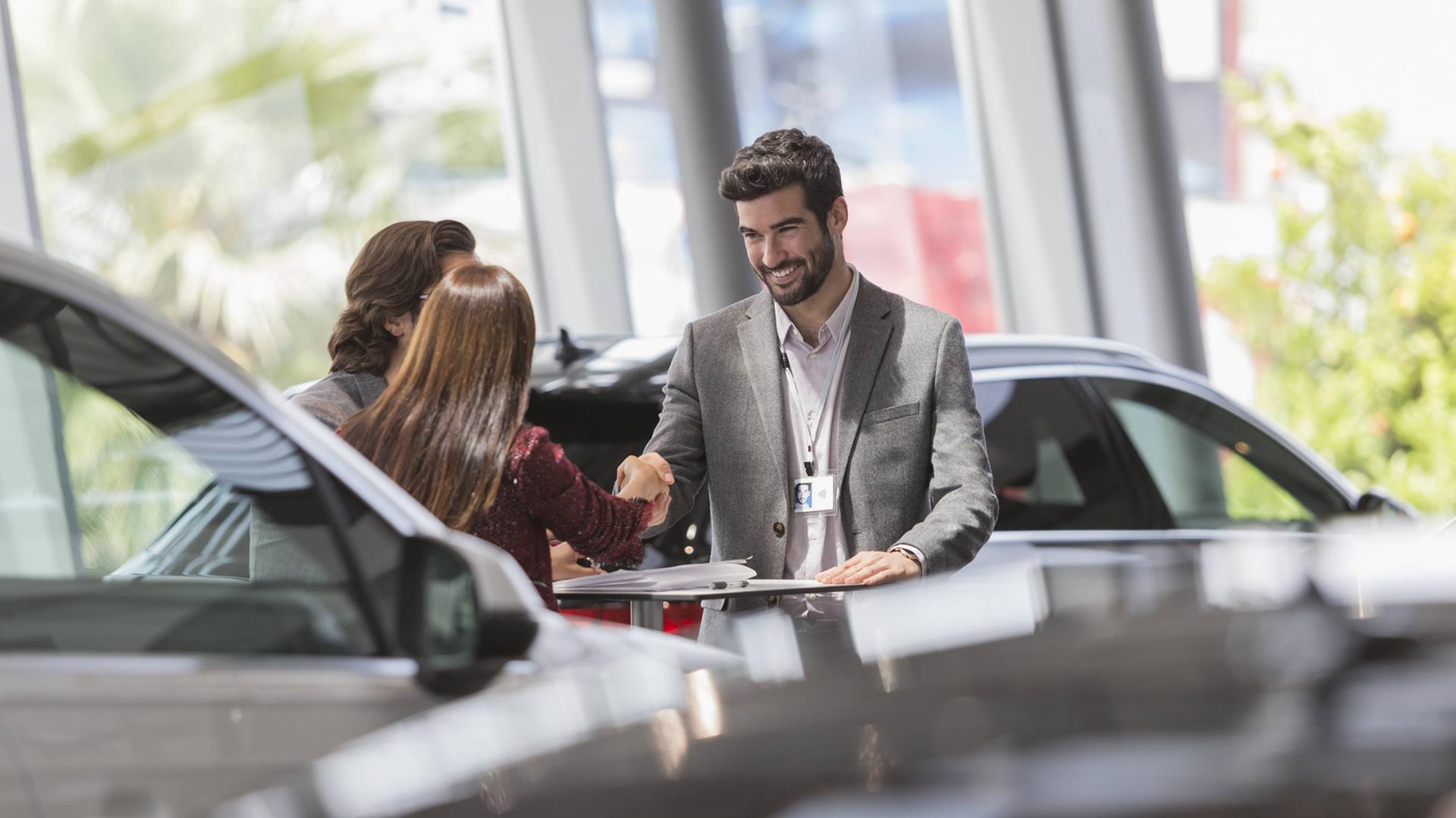 Ein Autoverkäufer schüttelt die Hände seiner Kunden - mit einem Lächeln im Gesicht. Ein Autoverkäufer schüttelt die Hände seiner Kunden - mit einem Lächeln im Gesicht.