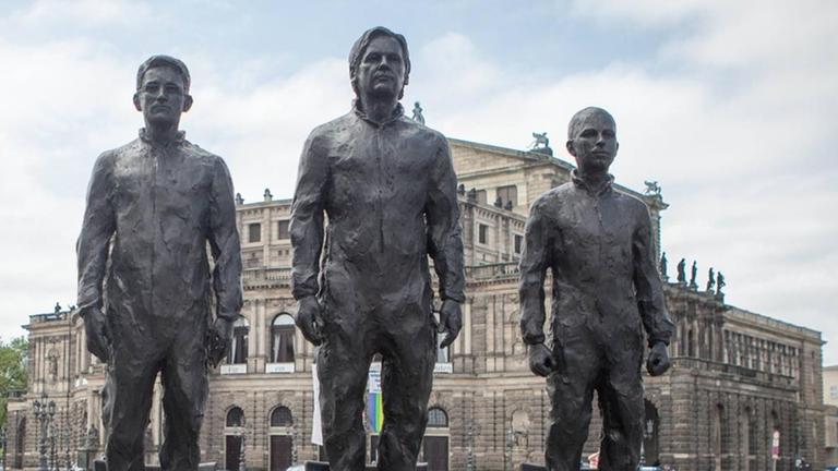 Bronzeskulpturen sind aufgebaut und stehen auf drei Stühlen (Snowden, Assange, Manning). Ganz links steht der Künstler Davide Domino. Bronzeskulpturen sind aufgebaut und stehen auf drei Stühlen (Snowden, Assange, Manning). Ganz links steht der Künstler Davide Domino.