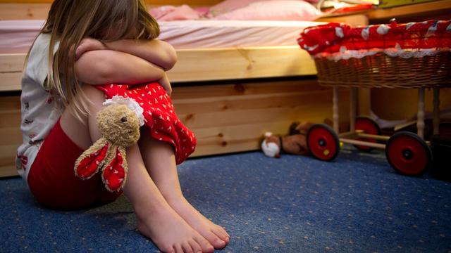 Ein kleines Mädchen sitzt weinend auf dem Fußboden in seinem Zimmer.