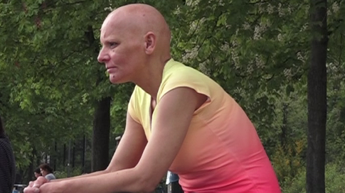 Ex-Turnerin Dana Boldt sitzt auf einer Steintreppe, ist seitlich zu sehen, ihr Blick geht nach links. Sie hat eine Glatze, hat männliche Züge und trägt ein Sportshirt, bei dem die Farbe oben von gelb ins Rötliche-Pinke übergeht. Außerdem eine lange schwarze Sporthose. Ex-Turnerin Dana Boldt sitzt auf einer Steintreppe, ist seitlich zu sehen, ihr Blick geht nach links. Sie hat eine Glatze, hat männliche Züge und trägt ein Sportshirt, bei dem die Farbe oben von gelb ins Rötliche-Pinke übergeht. Außerdem eine lange schwarze Sporthose.