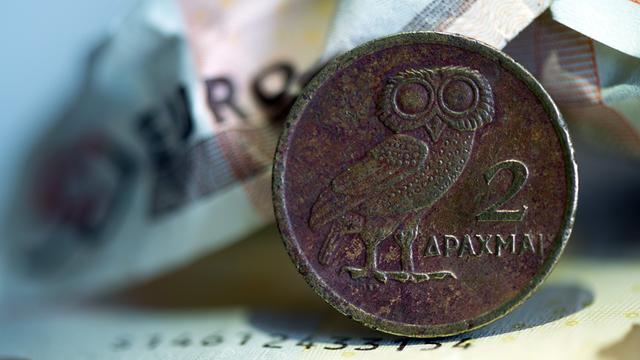 Eine griechische Drachmenmünze liegt auf geknüllten Euroscheinen.