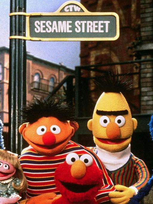 Die Puppen der Kindersendung Sesamstraße, das Krümelmonster, Mariechen, Ernie, Elmo, Bert und Grobi stehen vor einem Straßenschild mit der Aufschrift "Sesame Street"
