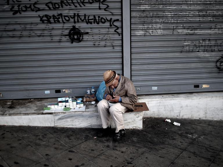 Ein älterer Mann verkauft Taschentücher vor einem geschlossenen Geschäft in Athen.