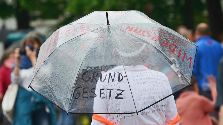 Teilnehmerin einer "Corona-Leugner" Demonstration in Heidelberg. Sie hält einen mit den Worten "Grundgesetz" und "Widerstand" beschriebenen Regenschirm.