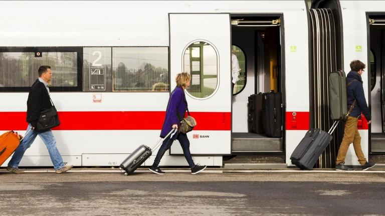 Passagiere laufen mit Koffern auf einem Bahnsteig vor einem ICE in Richtung einer geöffneten Zugtür.