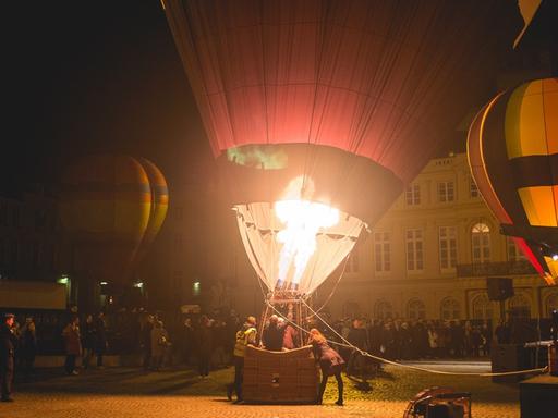 nächtliche Szene auf einem Platz, wo vor Publikum Heizluftballon gestartet werden