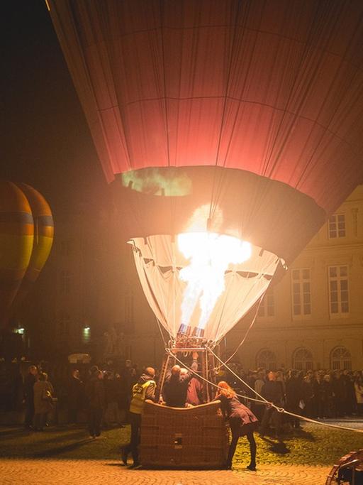 nächtliche Szene auf einem Platz, wo vor Publikum Heizluftballon gestartet werden