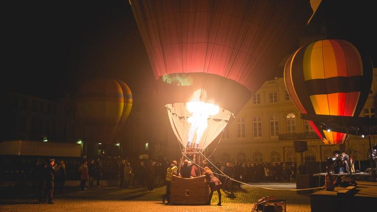 nächtliche Szene auf einem Platz, wo vor Publikum Heizluftballon gestartet werden nächtliche Szene auf einem Platz, wo vor Publikum Heizluftballon gestartet werden