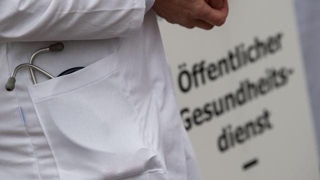 Ein Arzt steht vor einem Schild mit der Aufschrift "Öffentlicher Gesundheitsdienst".