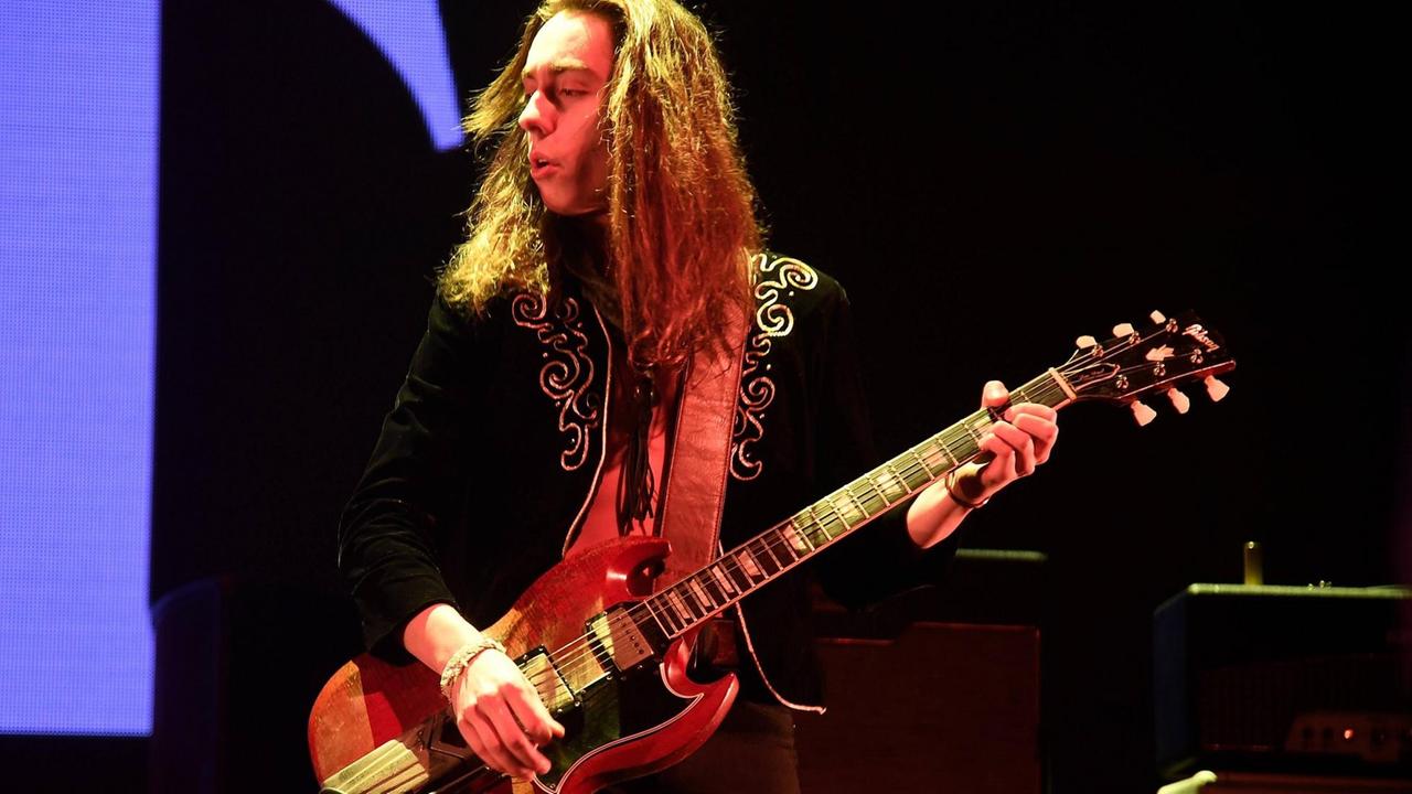 Ein Mann im bestickter Jacke steht auf einer Bühne und spielt Gitarre. Ein Mann im bestickter Jacke steht auf einer Bühne und spielt Gitarre.