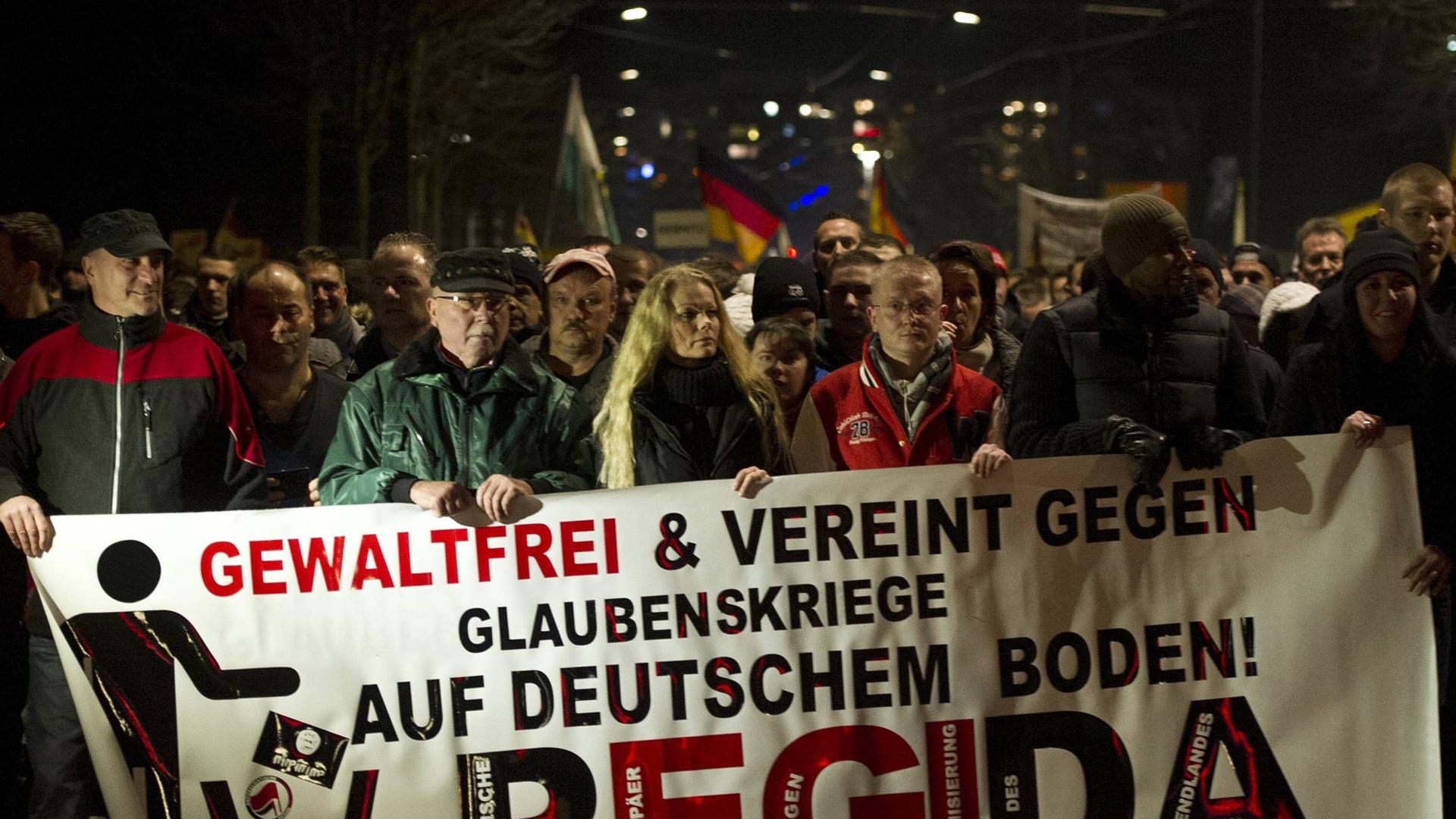 Mehrere Pegida-Demonstranten halten ein Banner mit der Aufschrift "Gewaltfrei und vereint gegen Glaubenskriege auf deutschem Boden!" Mehrere Pegida-Demonstranten halten ein Banner mit der Aufschrift "Gewaltfrei und vereint gegen Glaubenskriege auf deutschem Boden!"