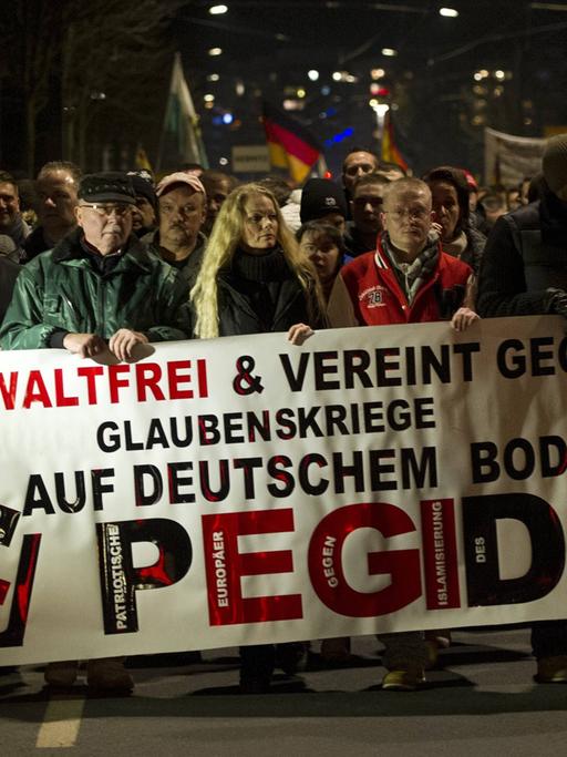 Mehrere Pegida-Demonstranten halten ein Banner mit der Aufschrift "Gewaltfrei und vereint gegen Glaubenskriege auf deutschem Boden!"