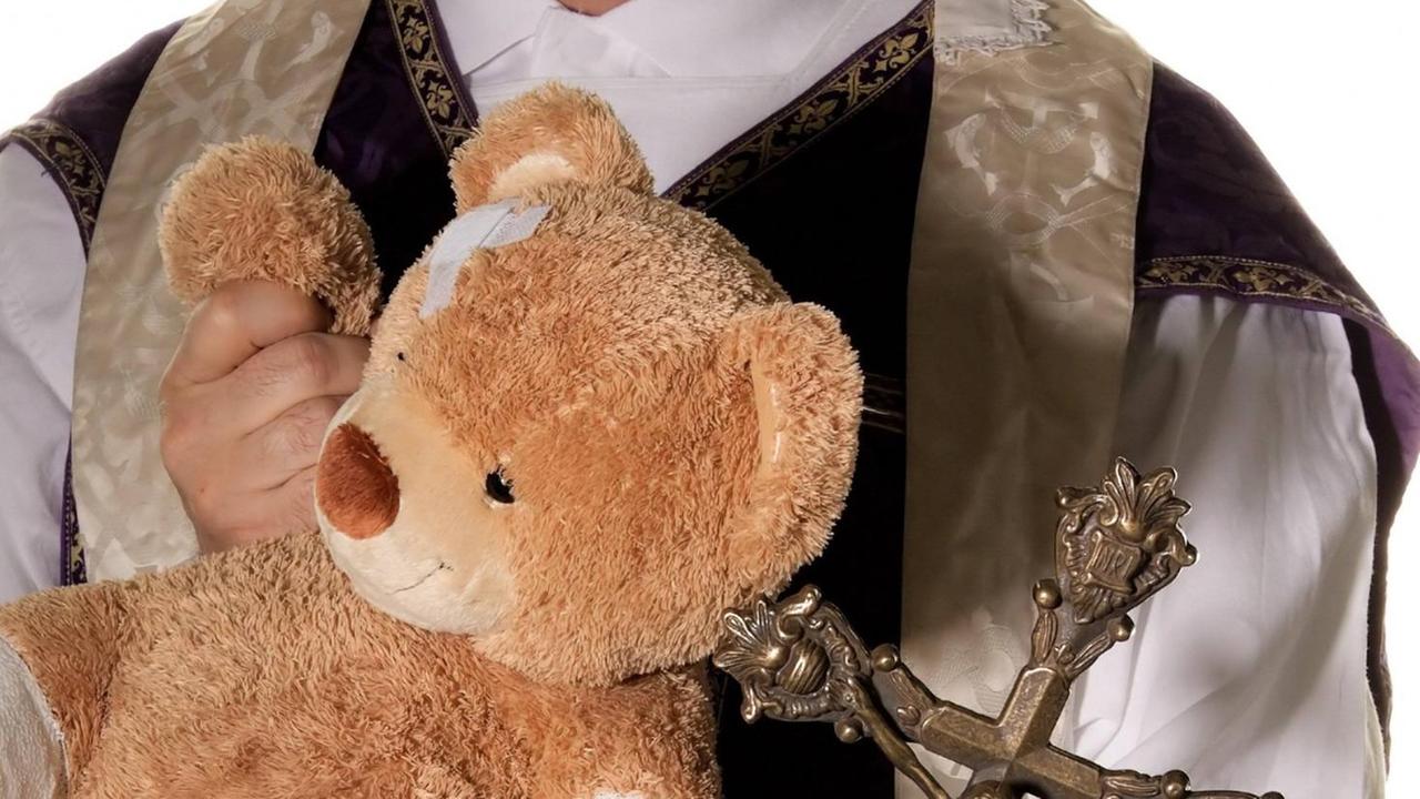 Ein Priester mit einem Teddybären, der ein Pflaster am Kopf hat