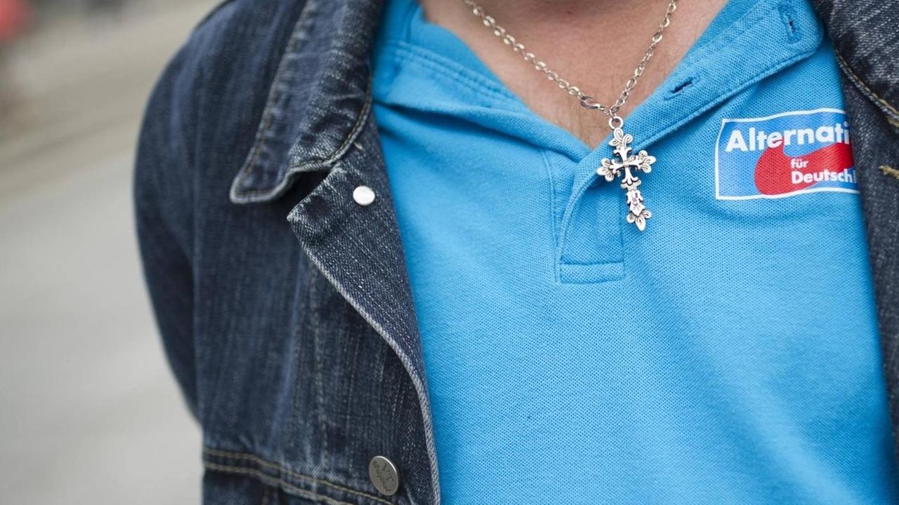 Ein Besucher einer Wahlveranstaltung der Partei Alternative für Deutschland (AfD) trägt eine Kette mit einem Kreuz und ein blaues T-Shirt mit dem Logo der AfD. Ein Besucher einer Wahlveranstaltung der Partei Alternative für Deutschland (AfD) trägt eine Kette mit einem Kreuz und ein blaues T-Shirt mit dem Logo der AfD.