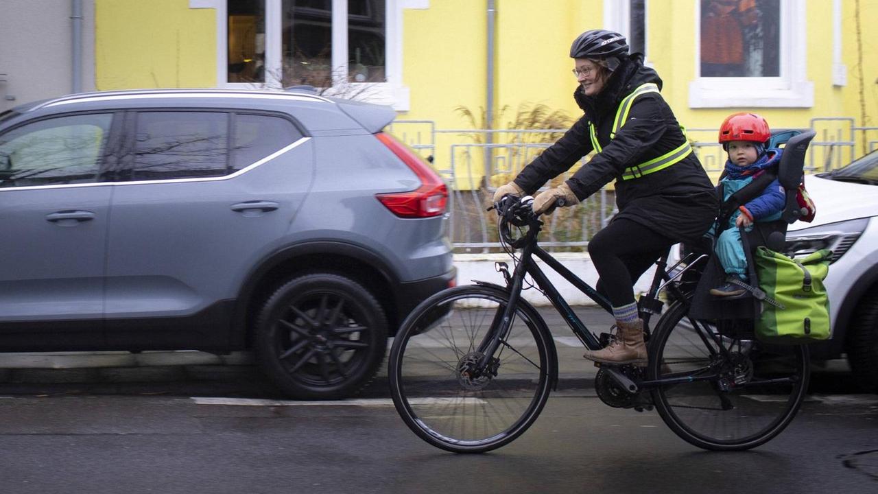 Eine Frau fährt mit einem Kind auf dem Rad durch eine ruhige Nebenstraße. Frau und Kind tragen Helm. Eine Frau fährt mit einem Kind auf dem Rad durch eine ruhige Nebenstraße. Frau und Kind tragen Helm.